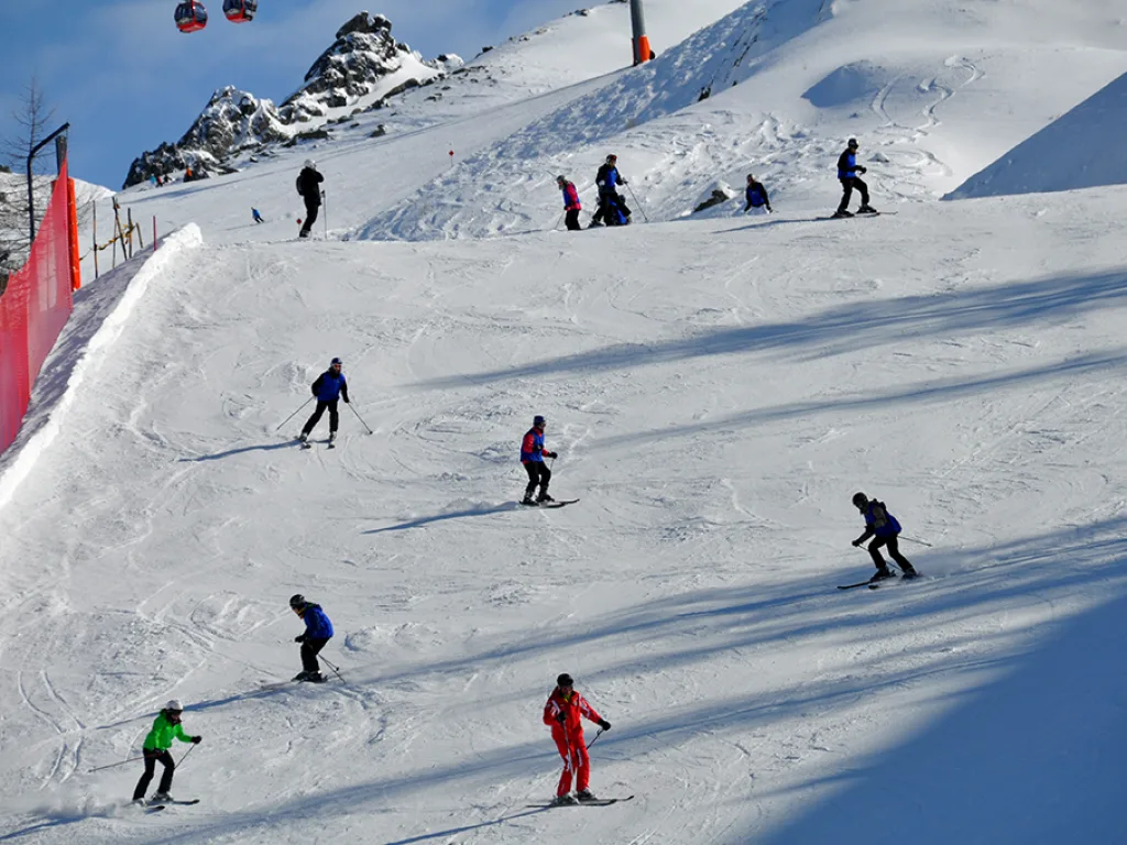 Mehrere Fahrende auf einer sonnigen Piste an einem Steilhang.